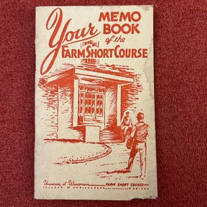 Pode incluir: Livro de memorandos vintage intitulado "Your Memo Book of the Farm Short Course" com ilustrações em vermelho e branco. A capa apresenta um edifício e figuras, com texto da Universidade de Wisconsin.