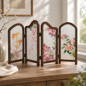 Könnte beinhalten: Ein vierflügeliger Raumteiler mit einem dunkelbraunen Holzrahmen und strukturierten Glaseinsätzen. Jeder Flügel zeigt eine eigene Blumenillustration, darunter orangefarbene Lilien, rosa Glyzinien, lila Flieder und rosa Blüten.