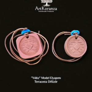 Puede incluir: Dos difusores de terracota con diseño de estrella, suspendidos por cordones marrones y detalles azules. Uno es cuadrado, el otro redondo. La imagen incluye el texto "ArtKoranza Handmade Products" y "Yıldız Model Elyapımı Terracotta Difüzör."