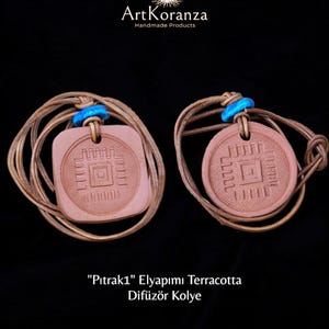 Op de afbeelding: Twee terracotta hangers met een geometrisch ontwerp, elk opgehangen aan een bruin koord en een blauwe kraal. Eén hanger is vierkant, de andere rond. De tekst "ArtKoranza Handmade Products" staat bovenaan.