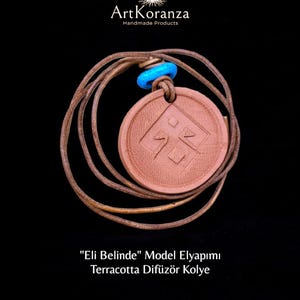 May include: A terracotta pendant necklace with a brown leather cord. The round pendant features an embossed geometric design and a blue bead. The image text reads "Eli Belinde" Model Elyapımı Terracotta Difüzör Kolye.