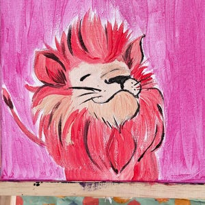 May include: A pink acrylic painting of a lion's face on a square canvas. The lion has a pink mane and a smiling expression. The background is a solid pink color. The canvas is on a wooden easel.