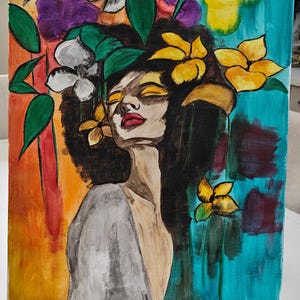 May include: An acrylic painting on canvas depicting a woman with closed eyes, adorned with flowers. The artwork features a vibrant color palette of yellow, orange, purple, and teal. The painting is displayed on a small wooden easel.