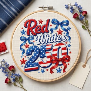 Pode incluir: Um bastidor de bordado de ponto cruz redondo com as palavras "Red White & 250" em vermelho, branco e azul. O design inclui estrelas e laços. O bastidor é rodeado por flores, tecido e uma etiqueta.