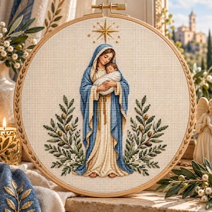 Pode incluir: Um bastidor de bordado circular de madeira contendo um desenho em ponto cruz de uma figura com túnica azul e creme segurando um bebé. Acima das figuras há uma estrela dourada e em ambos os lados ramos de oliveira verdes com azeitonas.