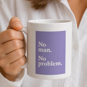 Könnte beinhalten: Weiße Keramik-Tasse mit dem Text "No man. No problem." in Weiß auf einem lila Hintergrund. Die Tasse hat einen gebogenen Henkel und wird von einer Person gehalten.
