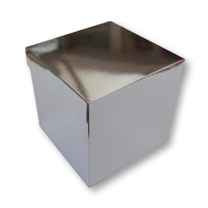 May include: A square gift box with a reflective, metallic silver finish. The box features a smooth, shiny surface that catches light, creating a mirror-like appearance on the top lid and the four vertical sides of the container structure.