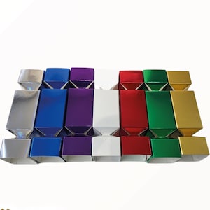 May include: A set of seven rectangular party crackers arranged in a row, featuring a metallic finish in silver, blue, purple, white, red, green, and gold. Each cracker has a central rectangular body with tapered ends and square-shaped openings.