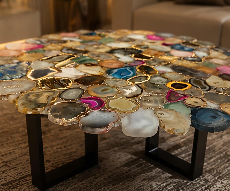 May include: A round coffee table with a mosaic top made of colorful agate slices. Each slice is outlined in gold and set on a black metal base. The table's design features a variety of colors, including blue, pink, and green.