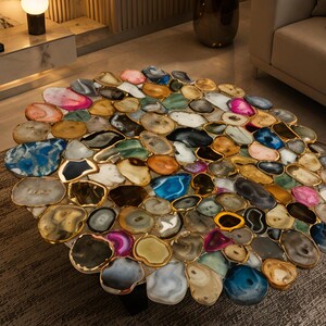 May include: A round coffee table with a mosaic top made of polished agate slices in various colors, including blue, pink, and gold. The agate slices are framed with gold-colored metal. The table is a unique piece of furniture.