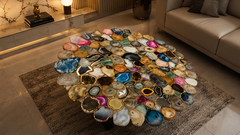 May include: A round coffee table with a mosaic top made of polished agate slices in various colors, including blue, pink, and gold. The agate slices are framed with gold-colored metal. The table is a unique piece of furniture.