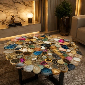 May include: A round coffee table with a mosaic top made of various colorful agate slices. The agate pieces are framed with gold trim and set on a black metal base. The table is a unique piece of furniture.