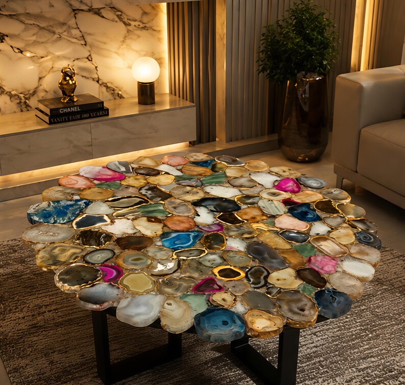 May include: A round coffee table with a mosaic top made of various colorful agate slices. The agate pieces are framed with gold trim and set on a black metal base. The table is a unique piece of furniture.