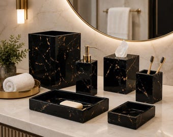 Puede incluir: Un juego de accesorios de baño con patrón de mármol negro y dorado. El conjunto incluye un cubo de basura, un dispensador de jabón con bomba dorada, una caja para pañuelos, un porta cepillos y dos bandejas con una pastilla de jabón.
