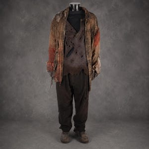 May include: A distressed costume ensemble featuring a brown, tattered jacket with reddish patches, layered over a dark brown, hole-riddled top and matching dark brown trousers. The outfit is completed with a pair of worn, brown, lace-up boots.