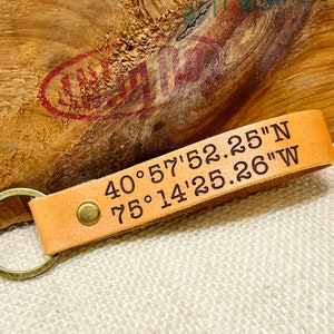 May include: A tan leather keychain with a brass ring and a metal rivet. The keychain has the coordinates "40&deg; 57' 52.25" N 75&deg; 14' 25.26" W" engraved on it.