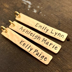 May include: Three gold-toned metal bar pendants with names engraved on them. The names are "Emily Lynn", "Ashleigh Marie", and "Kelly Paige".