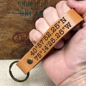 May include: A tan leather keychain with a metal ring and the coordinates "40.57'52.25"N 75.14'25.26"W" engraved on it.