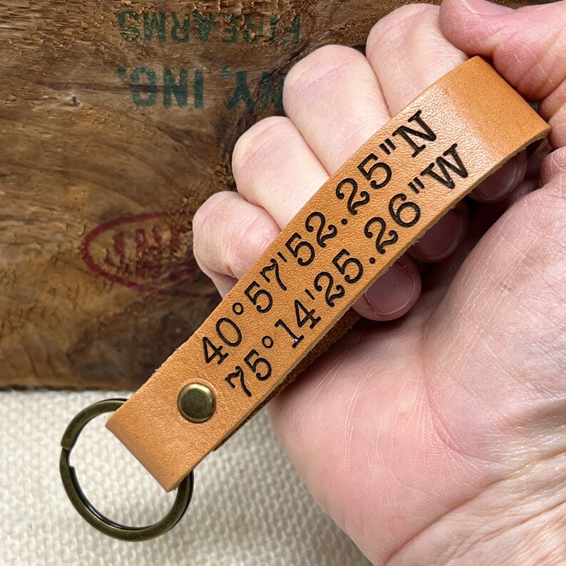 May include: A tan leather keychain with a metal ring and the coordinates "40.57'52.25"N 75.14'25.26"W" engraved on it.
