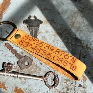 May include: A brown leather keychain with a key ring and engraved coordinates: "39&deg;26'39.876"N 83&deg;48'56.088"W".