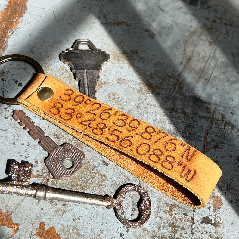 May include: A brown leather keychain with a key ring and engraved coordinates: "39&deg;26'39.876"N 83&deg;48'56.088"W".