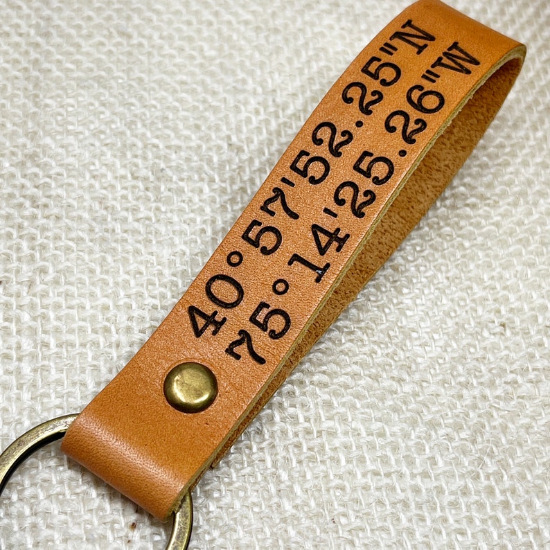 May include: A tan leather keychain with a brass ring and engraved coordinates: 40.57' 25.22'N 75.14' 22.26'W.