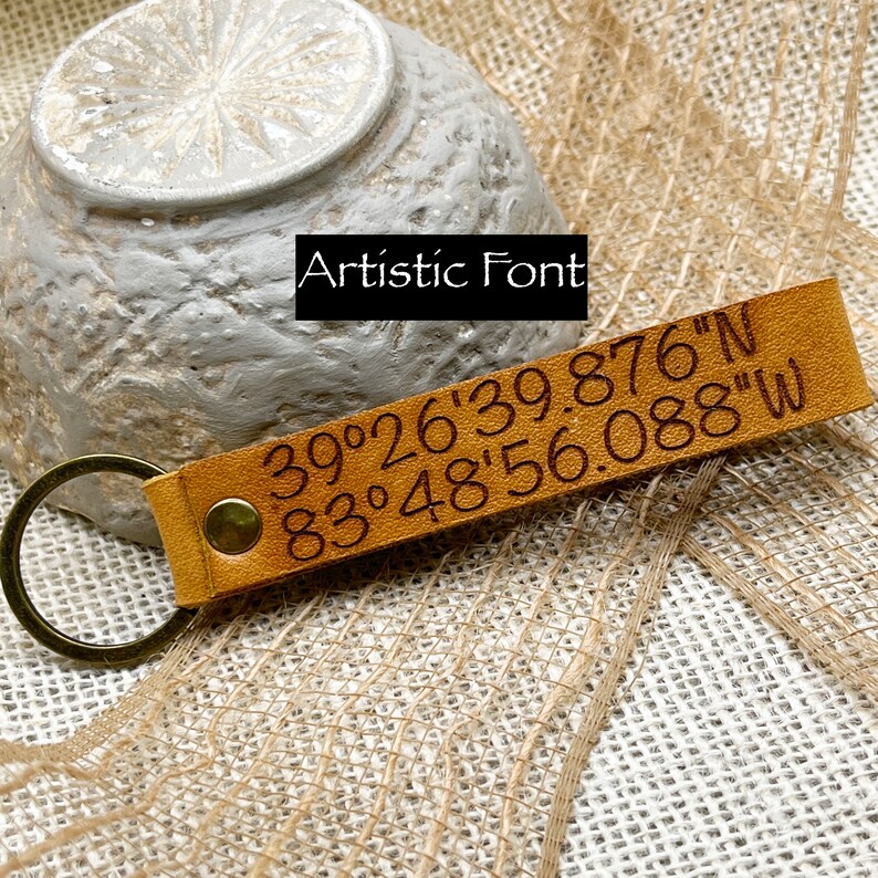 May include: A brown leather keychain with a brass ring and engraved coordinates: 39&deg;26'39.876"N 83&deg;48'56.088"W.