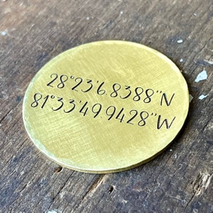 May include: A brass round disc with the coordinates 28°23'6.8388'N 81°33'49.9428'W engraved on it.