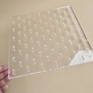 Könnte beinhalten: Transparente Acryl-Lochplatte mit zahlreichen länglichen Löchern. Die Löcher sind gleichmäßig über die Oberfläche verteilt. Die Platte ist klar und scheint unbenutzt zu sein. Die Platte wird von einer Hand gehalten.