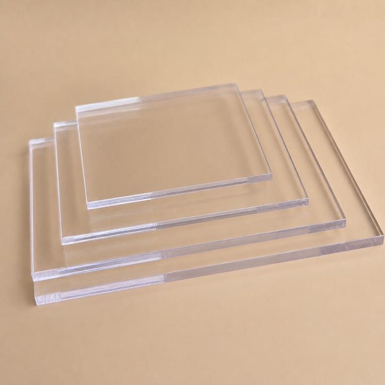 May include: Four clear, square acrylic sheets of varying sizes are stacked diagonally. The sheets are transparent, allowing light to pass through. The edges are smooth and the overall appearance is clean and modern.
