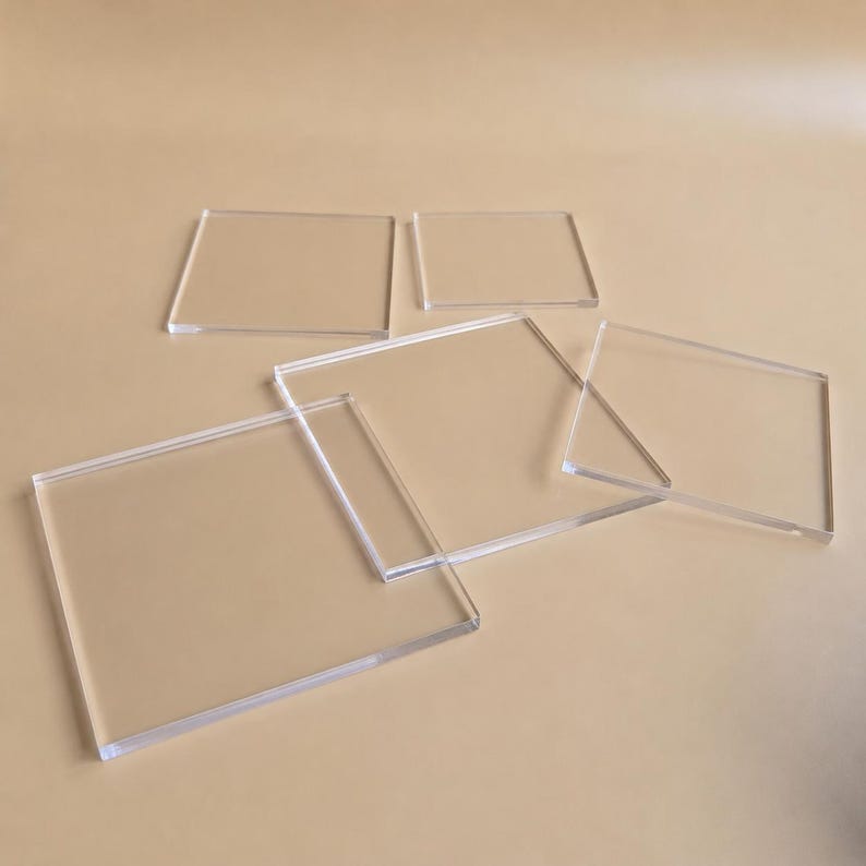 May include: Several clear, rectangular acrylic sheets of varying sizes are arranged on a neutral-toned surface. The transparent material allows the background color to show through, creating a subtle interplay of light and shadow. The sheets are slightly overlapping.