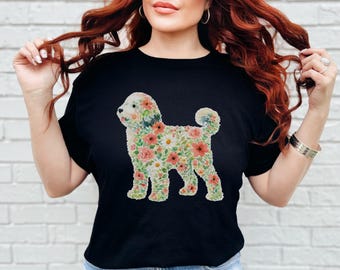 May include: A black short-sleeved t-shirt featuring a graphic print of a dog silhouette filled with a colorful pattern of various flowers and green leaves. The floral design includes shades of pink, red, white, and orange blossoms on a dark background.