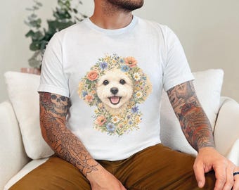 Puede incluir: Una camiseta blanca de manga corta con un gráfico central de la cara de un perro de color crema rodeada por un colorido arreglo de varias flores, incluyendo pétalos naranjas, azules y blancos. El perro tiene una expresión alegre.