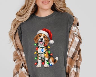 Könnte beinhalten: Ein anthrazitfarbenes T-Shirt mit Rundhalsausschnitt und einem Aufdruck eines Beagle-Welpen, der eine rot-weiße Weihnachtsmütze trägt und in eine Lichterkette mit bunten Weihnachtslichtern gewickelt ist. Das T-Shirt wird unter einem braun-weißen Flanellhemd getragen.