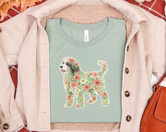 Puede incluir: Una camiseta de color verde salvia con el gráfico de la silueta de un perro relleno de un colorido patrón floral de flores rosas, naranjas y blancas con hojas verdes. El perro tiene la cara blanca con manchas negras en ojos y orejas.