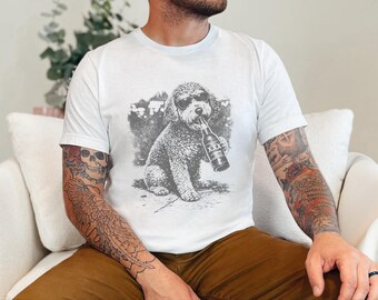 May include: A white short-sleeved t-shirt featuring a black and white graphic print of a curly-haired dog wearing sunglasses and holding a beer bottle labeled with three X symbols in its mouth. The design is centered on the chest area.