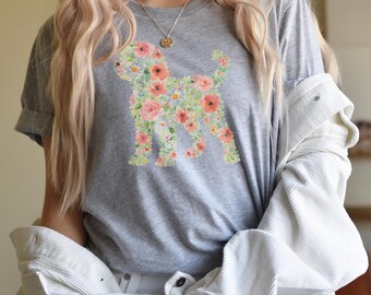 Puede incluir: Una camiseta gris jaspeado de manga corta con un estampado gráfico de la silueta de un perro relleno de un colorido patrón floral de flores rosas, naranjas y amarillas con hojas verdes, bajo una camisa de pana blanca con botones.