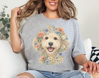 Puede incluir: Una camiseta gris jaspeado de manga corta con un gráfico central de la cara de un perro color crema rodeada por un colorido arreglo de diversas flores, incluyendo rosas rosadas, acianos azules y margaritas blancas en estilo artístico.