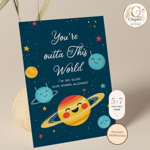 May include: A rectangular greeting card with a dark blue space background featuring colorful cartoon planets with smiling faces, stars, and the text: You're outta This World, I'M SO GLAD OUR STARS ALIGNED! The card is labeled 5 x 7 inches.