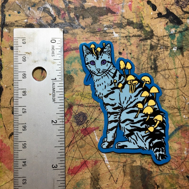 Op de afbeelding: Een blauwe kat met gele paddenstoelen die op zijn rug groeien. De kat zit op een blauwe achtergrond.