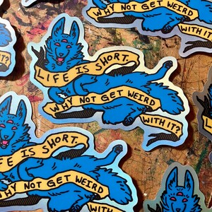 May include: A blue and yellow sticker with a cartoon dog with three eyes. The dog is holding a banner that says "Life is short. Why not get weird with it?"