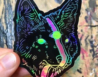 May include: A black and iridescent holographic sticker of a wolf's head with a pink tongue sticking out. The wolf's eyes are green and glow in the dark.