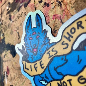 May include: A blue and yellow sticker with a cartoon wolf with three eyes and the text "Life is short don't not go"