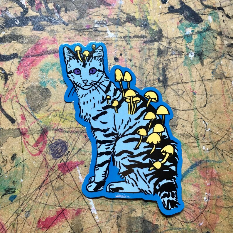 Op de afbeelding: Een blauwe en zwarte kat met gele paddenstoelen die op zijn rug groeien. De kat zit met zijn hoofd naar de zijkant gedraaid en zijn ogen dicht. De paddenstoelen bevinden zich in verschillende groeistadia, sommige zijn klein en andere zijn groot.