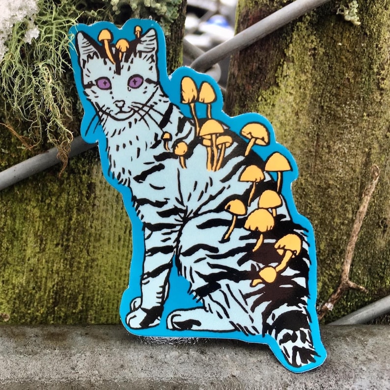 Op de afbeelding: Een blauwe en zwarte kat sticker met gele paddenstoelen die uit zijn rug groeien. De kat heeft paarse ogen en een witte streep op zijn voorhoofd.