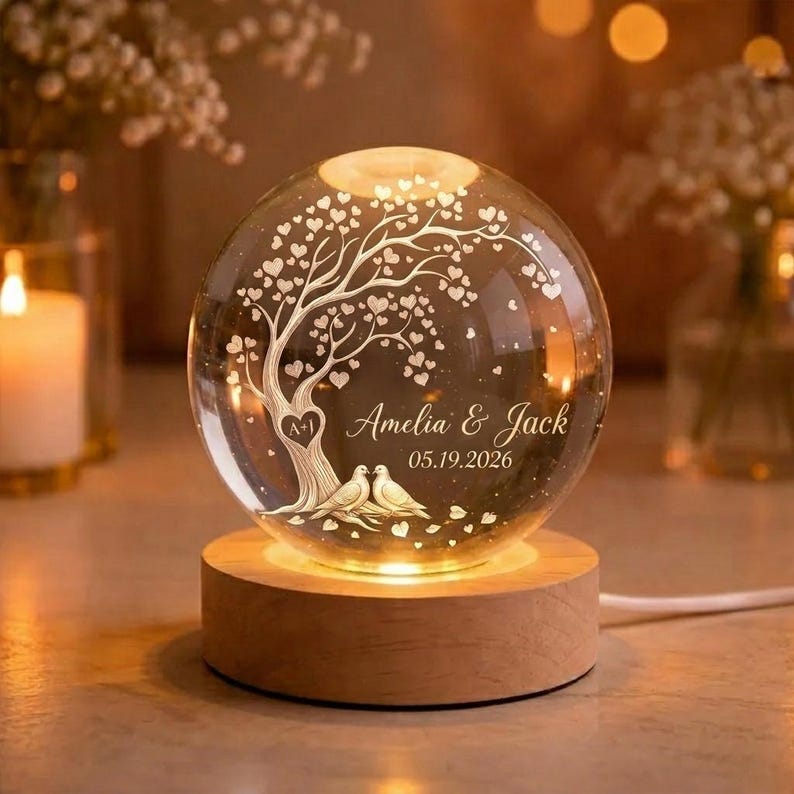 May include: A spherical glass night light on a round wooden base. The glass features an etched design of a tree with heart-shaped leaves, two birds at the base, and the text Amelia & Jack 05.19.2026 with a heart containing the letters A+I.