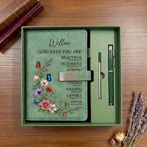Könnte beinhalten: Ein salbeigrünes Notizbuch-Set mit Magnetverschluss und passendem Stift. Der Einband zeigt den Namen Willow, den Text God Says You Are Beautiful, Victorious, Strong, Chosen, Amazing, Capable, Loved sowie ein Blumenmotiv mit Schmetterlingen.