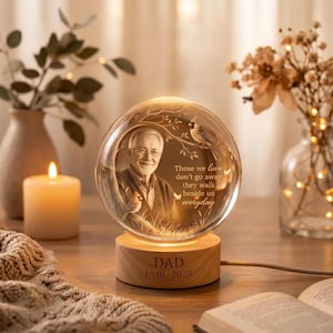 May include: A spherical glass night light featuring an engraved portrait of an older man, a cardinal bird on a branch, and the text: Those we love don't go away they walk beside us everyday. The base is wood with DAD 1948-2025 engraved on it.