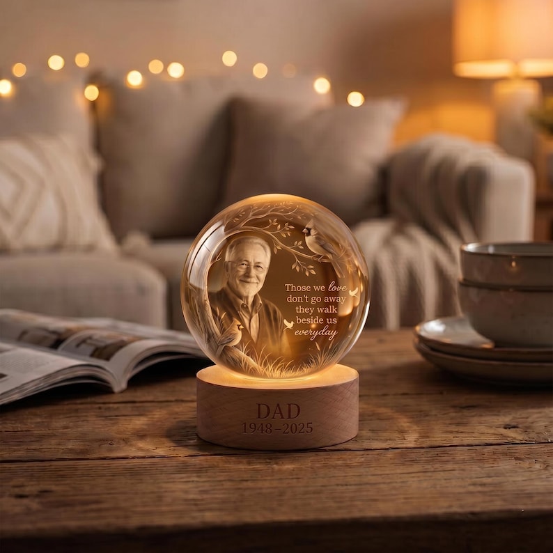 May include: A spherical glass memorial lamp featuring an etched portrait of a man, a tree, and a bird, with the text "Those we love don't go away they walk beside us everyday". The light sits on a wooden base engraved with "DAD 1948-2025".