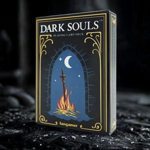 以下が含まれることがあります： 「DARK SOULS」と「PLAYING CARD DECK」の白い文字が入った黒いトランプの箱。箱には、三日月の下で焚き火の中の剣を描いた青と黒のイラストが描かれています。「fangamer」のロゴが下部にあります。